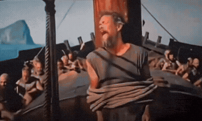 A Man With A Beard Is Tied To A Pole In Front Of A Boat GIF