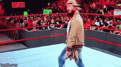 A Man With A Beard Is Walking In A Wrestling Ring With A Crowd Behind Him . GIF