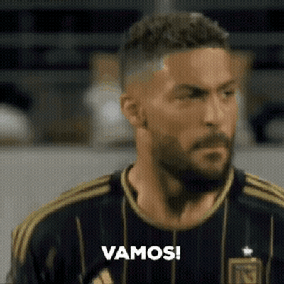 A Man With A Beard Is Wearing A Black And Gold Jersey And Says Vamos ! GIF