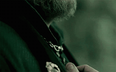 A Man With A Beard Is Wearing A Black Coat With A Gold Buckle . GIF