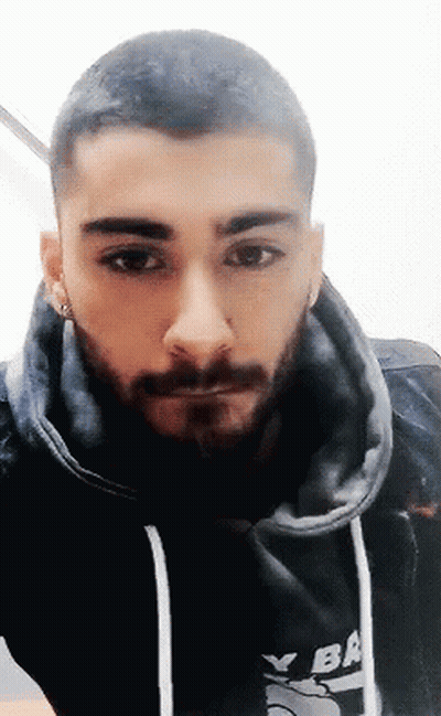 A Man With A Beard Is Wearing A Black Hoodie And Earrings . GIF
