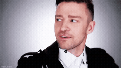 A Man With A Beard Is Wearing A Black Jacket And White Shirt And Making A Funny Face . GIF