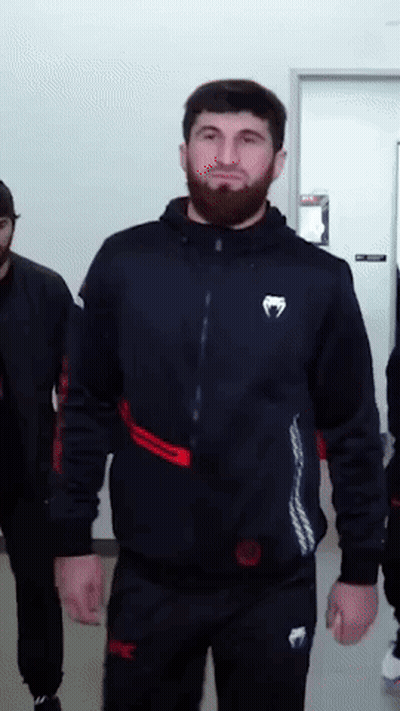 A Man With A Beard Is Wearing A Black Jacket With A White Venum Logo On The Front GIF