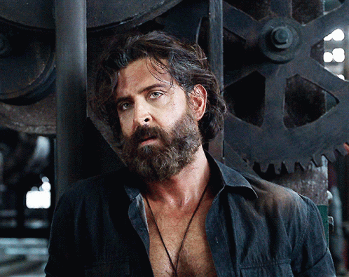 A Man With A Beard Is Wearing A Black Shirt And A Necklace GIF