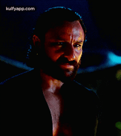 A Man With A Beard Is Wearing A Black Shirt And Looking At The Camera . GIF