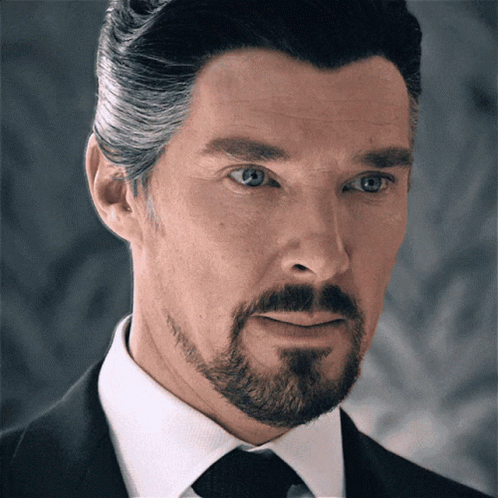 A Man With A Beard Is Wearing A Black Suit And Tie GIF