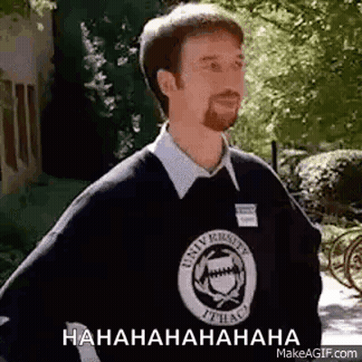 A Man With A Beard Is Wearing A Black Sweater And A White Shirt And Is Laughing . GIF