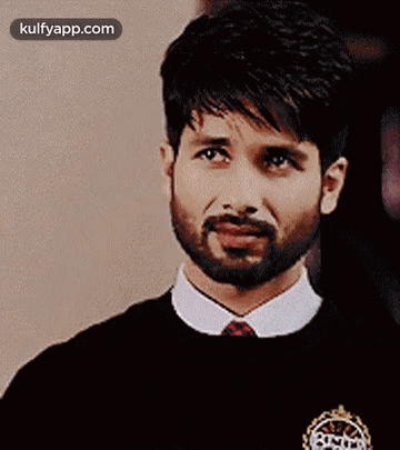 A Man With A Beard Is Wearing A Black Sweater And A White Shirt And Tie . GIF
