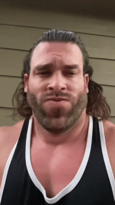 A Man With A Beard Is Wearing A Black Tank Top And Making A Funny Face GIF