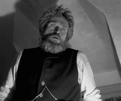A Man With A Beard Is Wearing A Black Vest And A Chain Around His Neck GIF