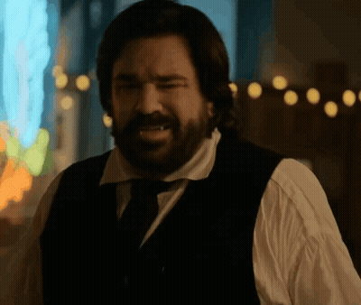 A Man With A Beard Is Wearing A Black Vest And Tie . GIF