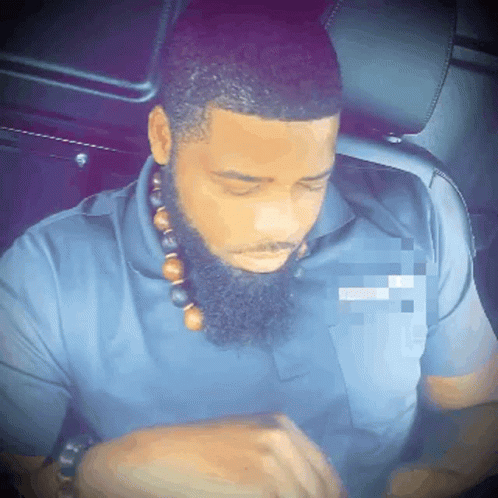 A Man With A Beard Is Wearing A Blue Shirt And A Necklace With Beads Around His Neck GIF