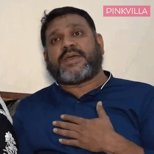 A Man With A Beard Is Wearing A Blue Shirt And Has His Hand On His Chest .. GIF