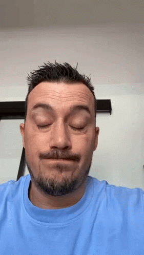 A Man With A Beard Is Wearing A Blue Shirt And Making A Funny Face GIF