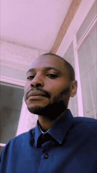 A Man With A Beard Is Wearing A Blue Shirt With Buttons On The Front GIF