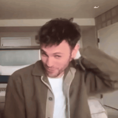 A Man With A Beard Is Wearing A Brown Jacket And White Shirt GIF