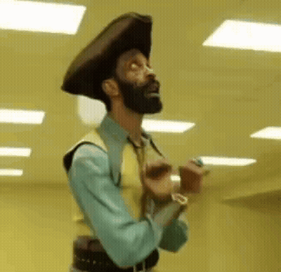 A Man With A Beard Is Wearing A Cowboy Hat And A Vest GIF