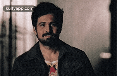 A Man With A Beard Is Wearing A Denim Jacket And A Tie . GIF