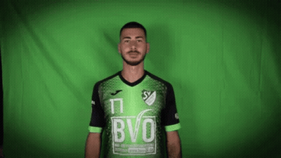 A Man With A Beard Is Wearing A Green And Black Soccer Jersey . GIF