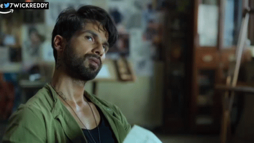 A Man With A Beard Is Wearing A Green Shirt And A Black Tank Top . GIF
