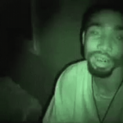 A Man With A Beard Is Wearing A Green Shirt And A Hat . GIF