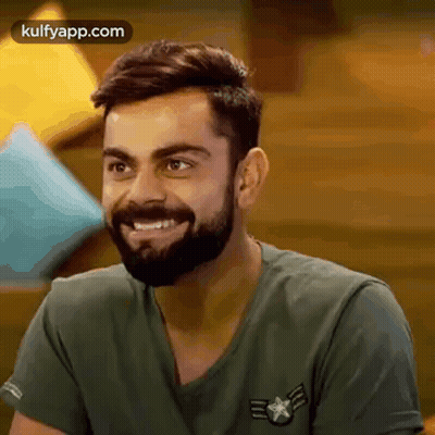 A Man With A Beard Is Wearing A Green Shirt And Smiling . GIF