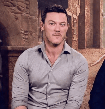 A Man With A Beard Is Wearing A Grey Shirt And Making A Face . GIF