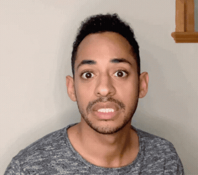 A Man With A Beard Is Wearing A Grey Shirt And Making A Funny Face GIF
