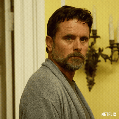 A Man With A Beard Is Wearing A Grey Sweater With A Netflix Logo On The Bottom GIF
