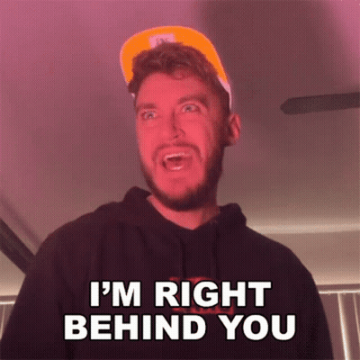 A Man With A Beard Is Wearing A Hat And A Hoodie And Says I 'M Right Behind You . GIF