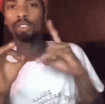 A Man With A Beard Is Wearing A Hat And A White Shirt And Making A Funny Face . GIF