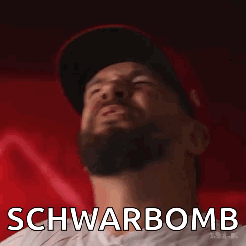 A Man With A Beard Is Wearing A Hat And Has The Word Schwarbomb Written On His Face GIF