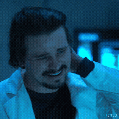 A Man With A Beard Is Wearing A Lab Coat And Smiling While Holding His Neck . GIF