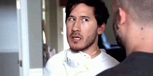 A Man With A Beard Is Wearing A Mask Around His Neck While Talking To Another Man GIF