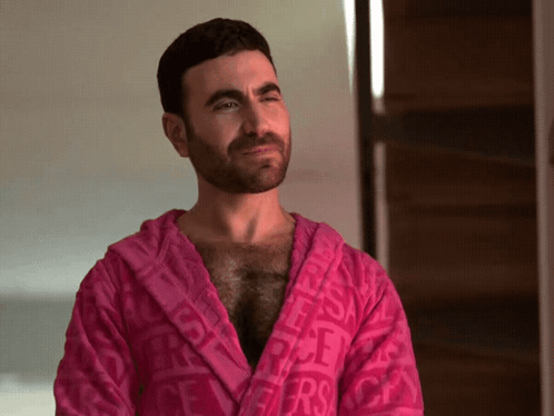 A Man With A Beard Is Wearing A Pink Robe With The Word Versace Printed On It GIF