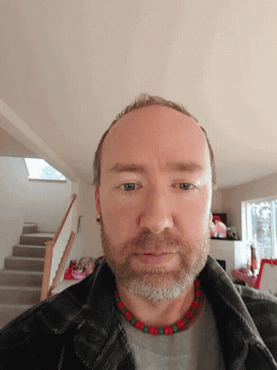 A Man With A Beard Is Wearing A Plaid Jacket And A Red And Green Necklace GIF