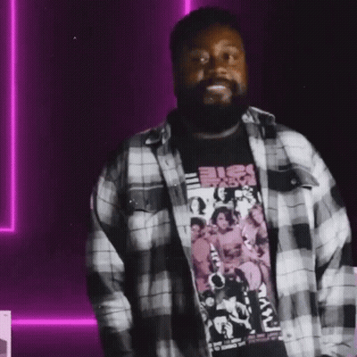A Man With A Beard Is Wearing A Plaid Shirt And A Black Shirt GIF