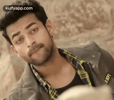 A Man With A Beard Is Wearing A Plaid Shirt And A Jacket And Looking At The Camera . GIF