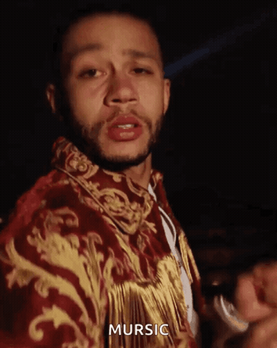 A Man With A Beard Is Wearing A Red And Gold Jacket With The Word Mursic On It . GIF
