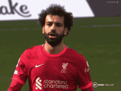 A Man With A Beard Is Wearing A Red Jersey That Says Standard Chartered GIF