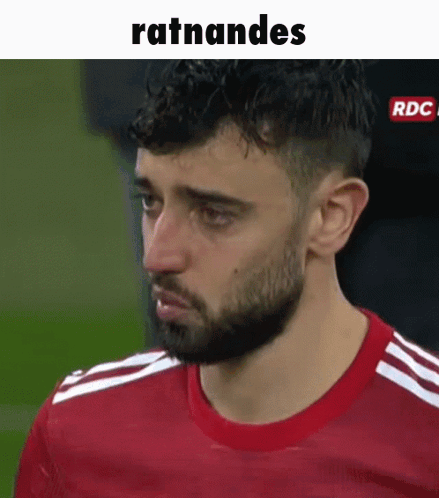 A Man With A Beard Is Wearing A Red Shirt And Making A Funny Face On A Soccer Field . GIF