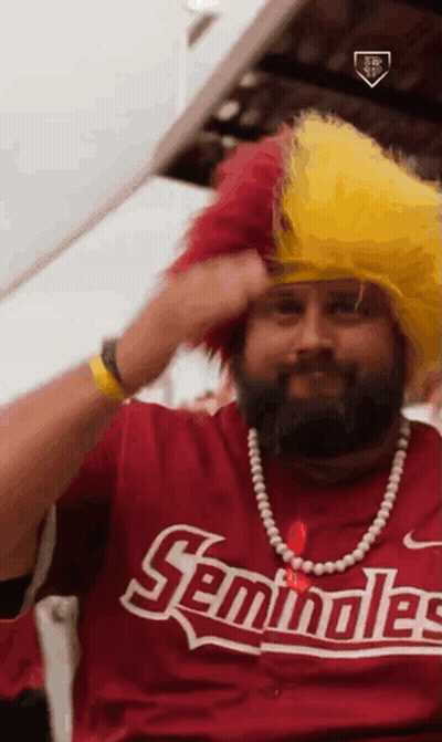 A Man With A Beard Is Wearing A Seminoles Shirt And A Yellow Wig GIF