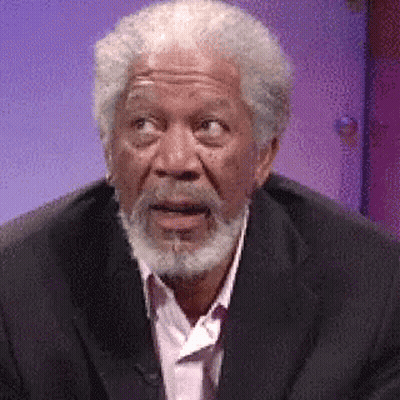 A Man With A Beard Is Wearing A Suit And A Pink Shirt And Making A Surprised Face . GIF