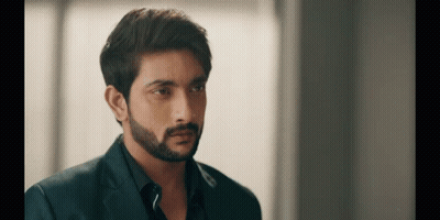 A Man With A Beard Is Wearing A Suit And Black Shirt And Looking At The Camera . GIF
