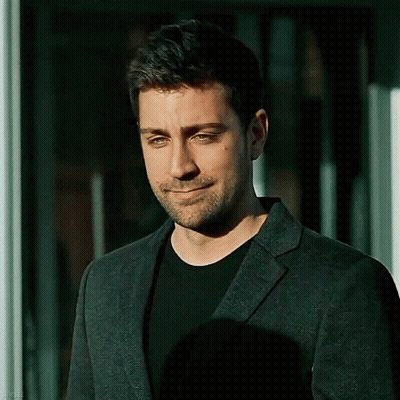 A Man With A Beard Is Wearing A Suit And Smiling . GIF