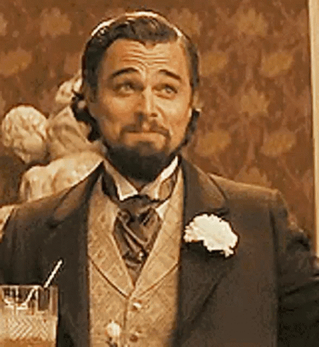 A Man With A Beard Is Wearing A Suit And Tie And Holding A Glass Of Water . GIF