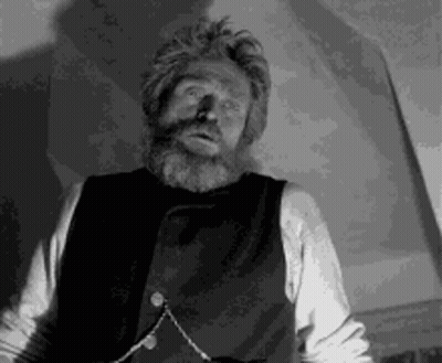 a man with a beard is wearing a vest and a chain around his neck .