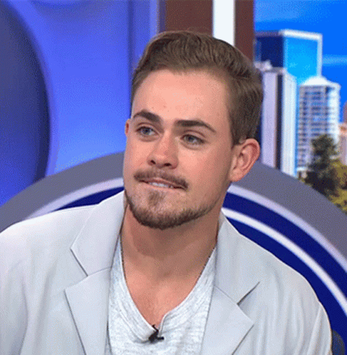 A Man With A Beard Is Wearing A White Jacket And Grey Shirt GIF