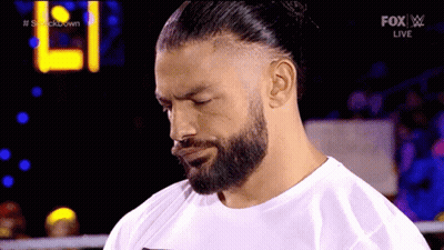 A Man With A Beard Is Wearing A White Shirt And A Bun . GIF
