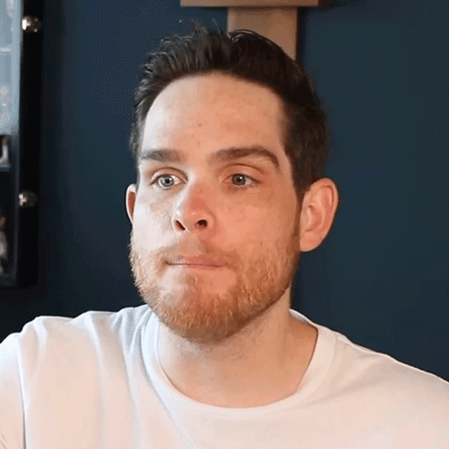 A Man With A Beard Is Wearing A White Shirt And Looking At The Camera GIF